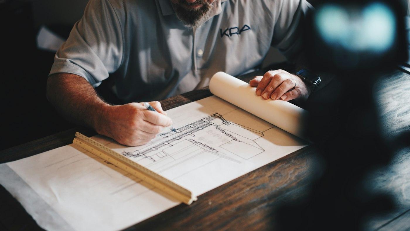 Hands drafting a site plan on a drawing board